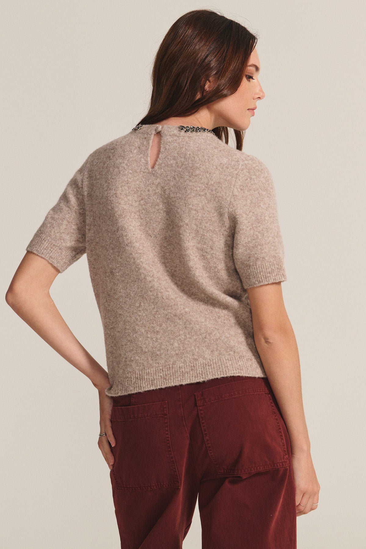 Woman stands with her back to the camera, wearing Velvet by Graham & Spencer's BRIANA SWEATER—a short-sleeve wool blend top with a back keyhole detail—paired with burgundy pants for a stylish cold-weather update.