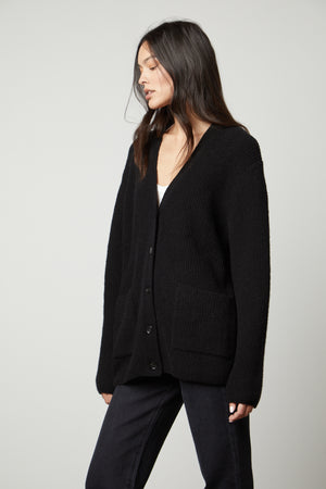 A woman wearing a black Velvet by Graham & Spencer BRITT OVERSIZED CARDIGAN and jeans.