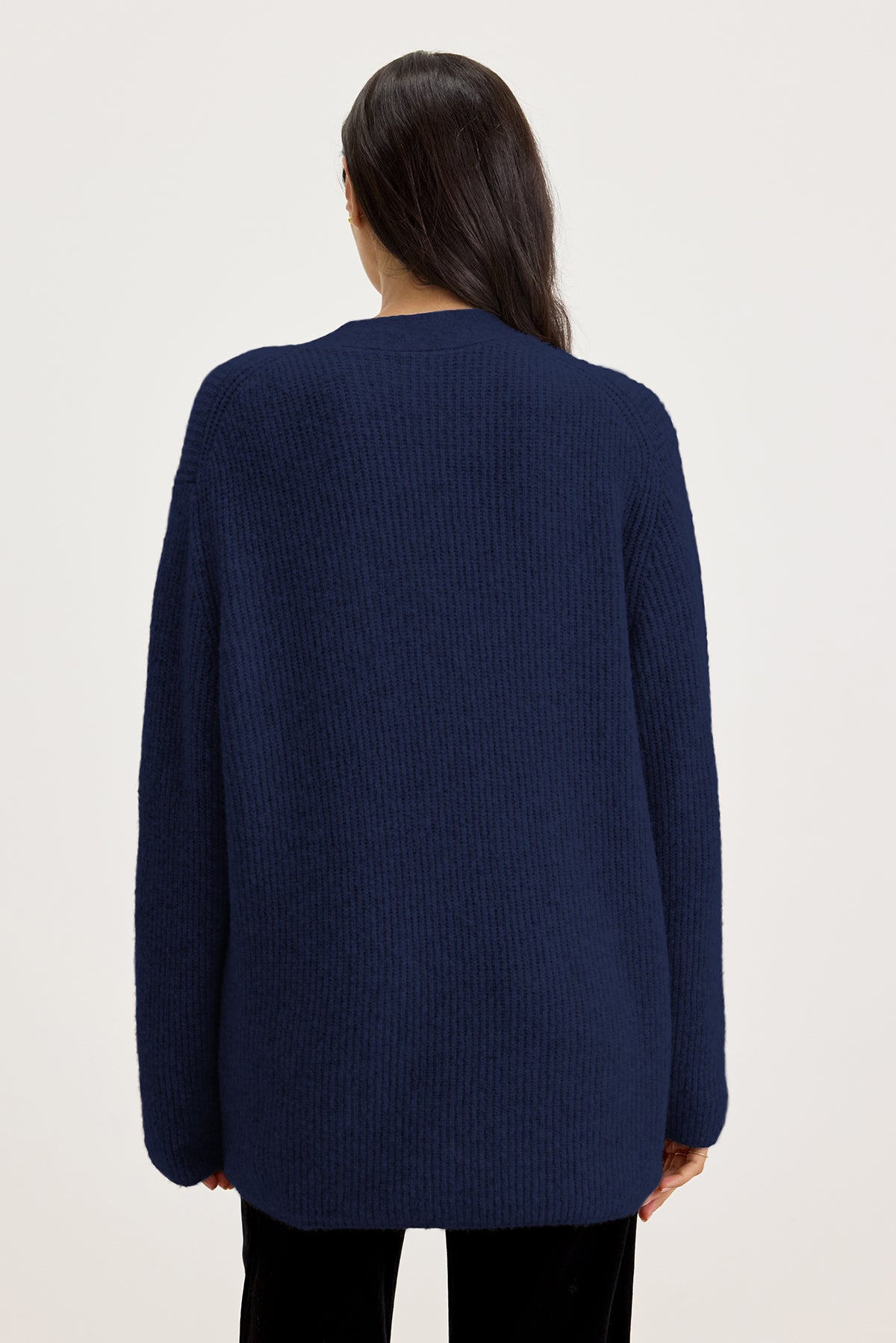   A person wearing the BRITT CARDIGAN, an oversized dark blue wool blend knit sweater from Velvet by Graham & Spencer, photographed from behind against a plain white background. 