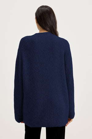 A person wearing the BRITT CARDIGAN, an oversized dark blue wool blend knit sweater from Velvet by Graham & Spencer, photographed from behind against a plain white background.