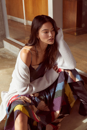 A woman is sitting on the floor in a colorful Velvet by Graham & Spencer BRITT OVERSIZED CARDIGAN.