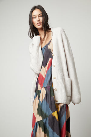 The model is wearing a multicolored dress and a Velvet by Graham & Spencer BRITT OVERSIZED CARDIGAN.