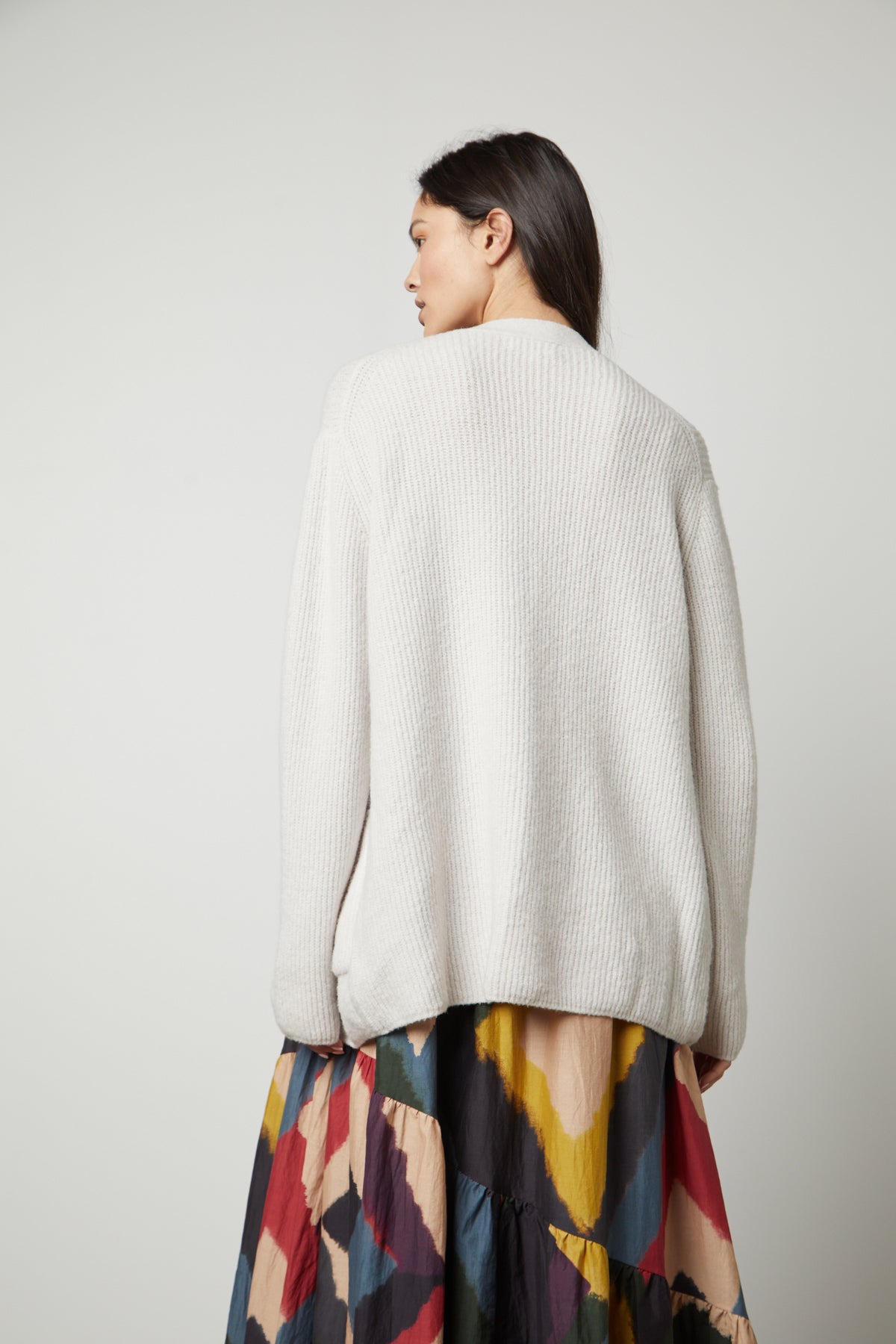   The back view of a woman wearing a Velvet by Graham & Spencer BRITT OVERSIZED CARDIGAN and multicolored skirt. 