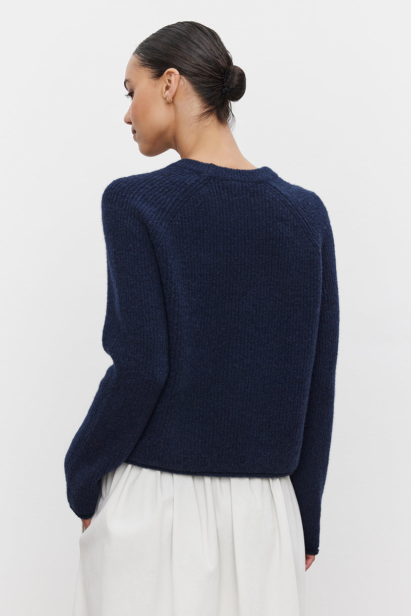 A person with their hair up in a bun is wearing the dark blue GIGI SWEATER by Velvet by Graham & Spencer along with a white skirt, viewed from the back.