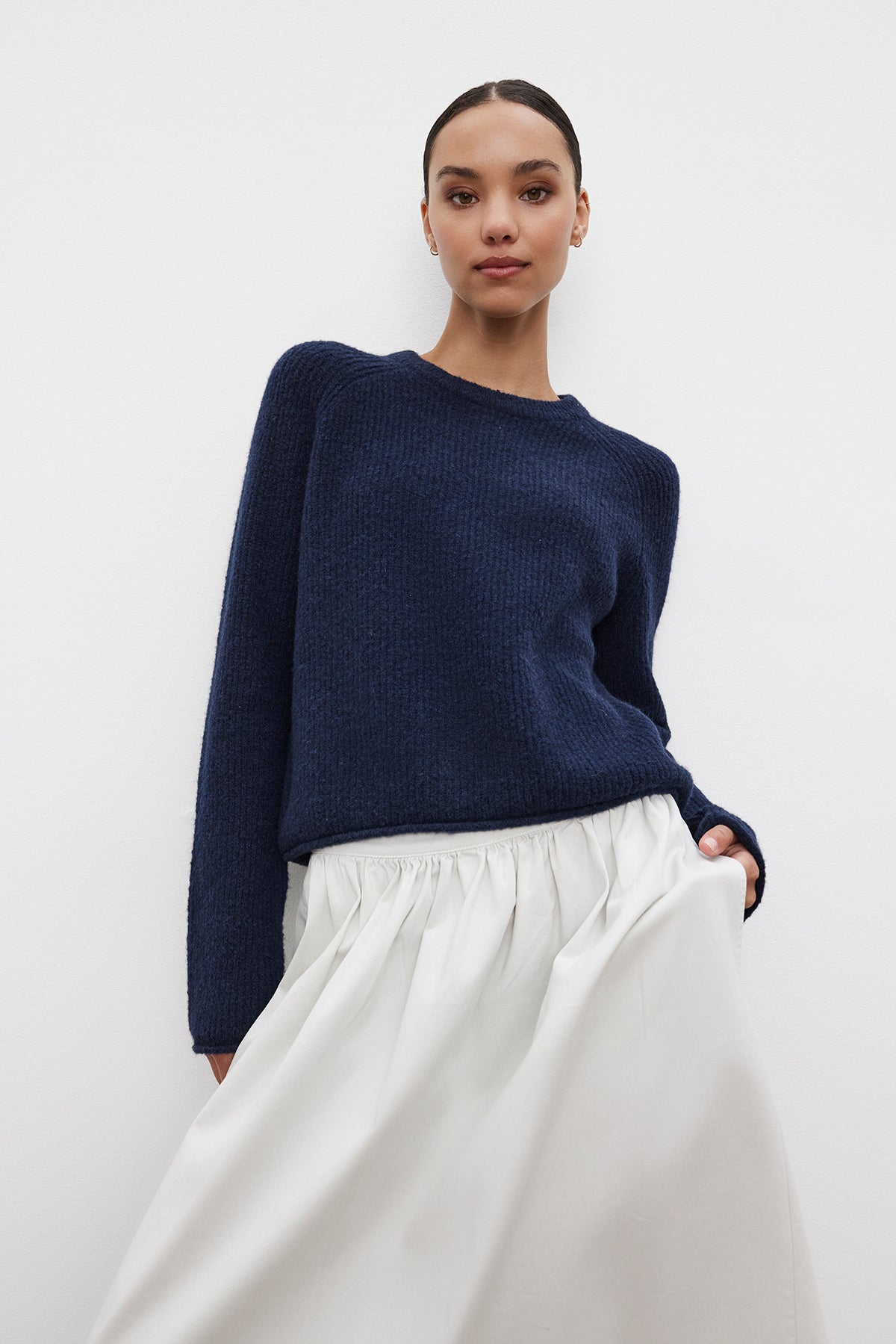   A person is wearing the Velvet by Graham & Spencer GIGI SWEATER in navy blue and a white skirt, posing against a plain white background. 