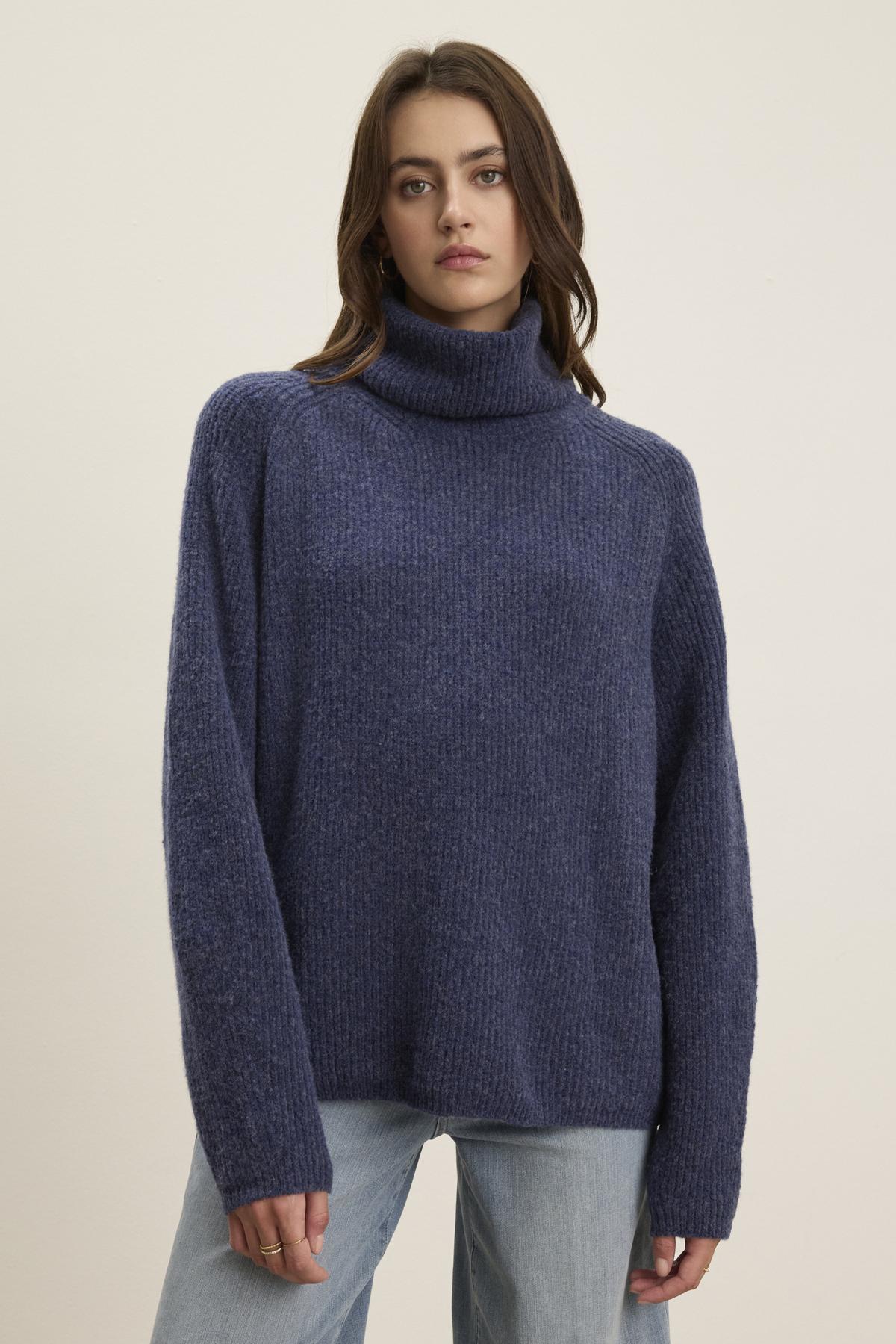   A person is wearing the JUDITH TURTLENECK SWEATER from Velvet by Graham & Spencer, styled with light blue jeans, standing against a plain background. 