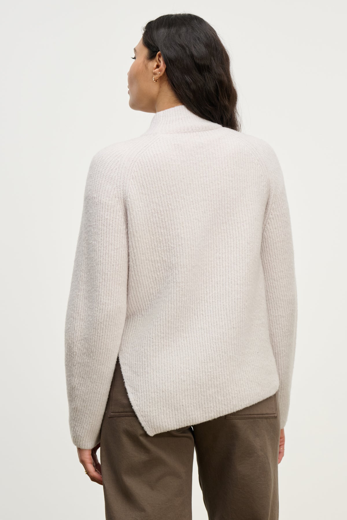 A woman is shown from behind wearing the LESA SWEATER by Velvet by Graham & Spencer, a light-colored, ribbed mock neck style, paired with brown pants against a plain background.-39838357684417