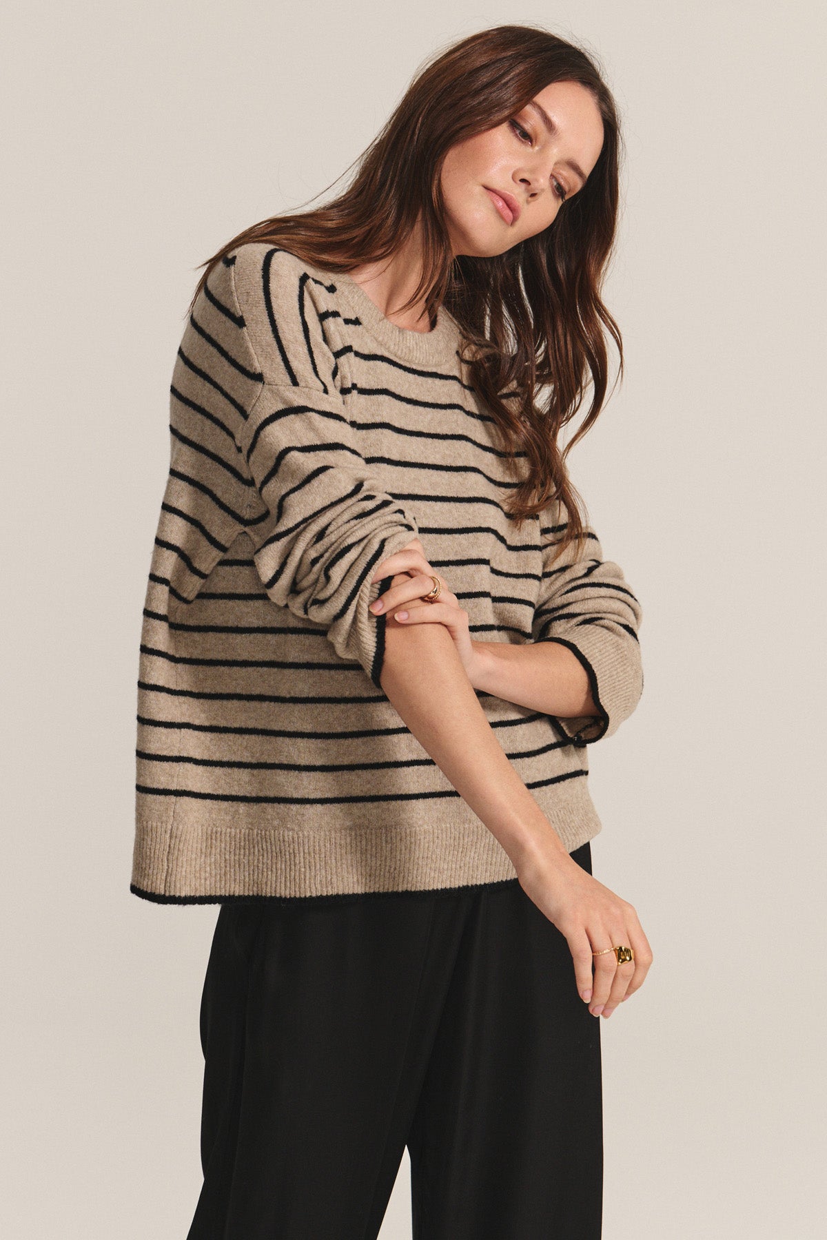 A woman wears the ROMY SWEATER by Velvet by Graham & Spencer, a cozy wool blend with black horizontal stripes, paired with black pants against a plain light background.-40672489832641