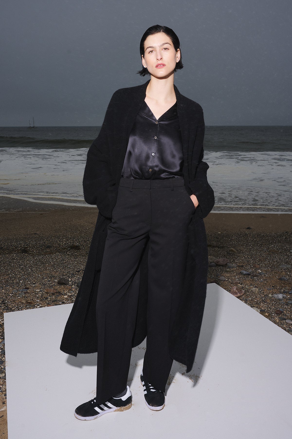   A woman in a black coat standing on the beach, wearing Velvet by Jenny Graham's PRINCE PANT straight-leg pants. 