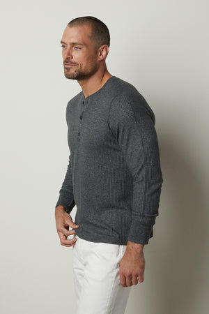 A man wearing a grey sweater and white pants with an Anthony Thermal Henley by Velvet by Graham & Spencer, featuring a classic waffle texture.