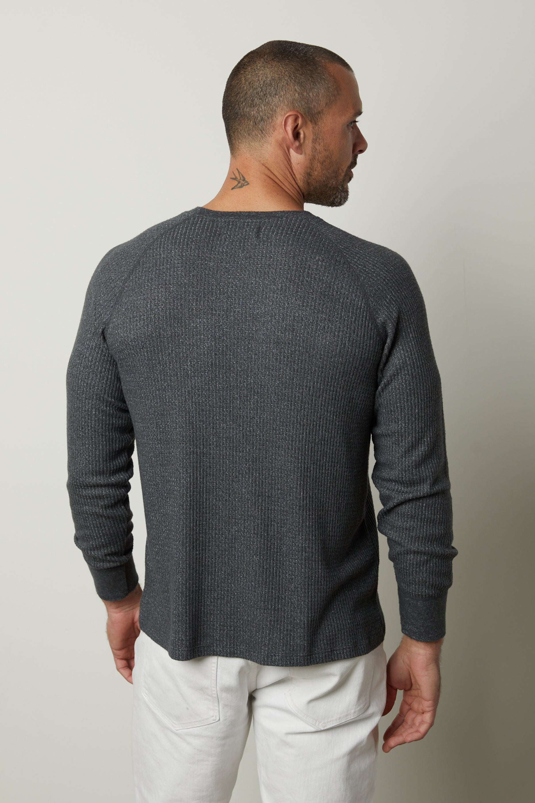   The back view of a man wearing a Velvet by Graham & Spencer Anthony Thermal Henley and white pants with a button-placket. 