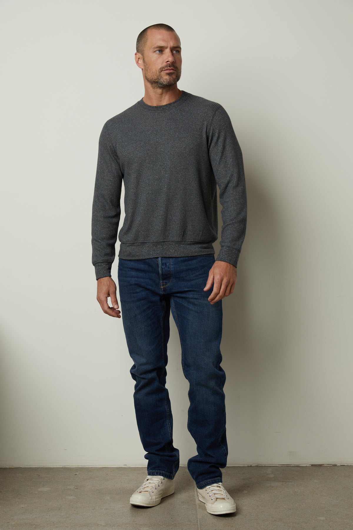 A man wearing jeans and a sweater in the PONCHO THERMAL CREW style by Velvet by Graham & Spencer standing in front of a wall.-35547551498433
