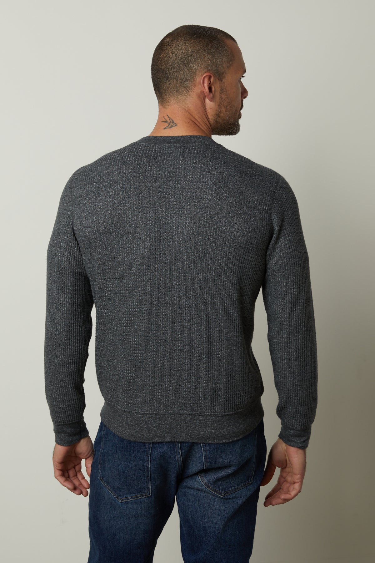 The back view of a man wearing a Velvet by Graham & Spencer PONCHO THERMAL CREW grey sweater and jeans, perfect for cooler days.-35547551563969