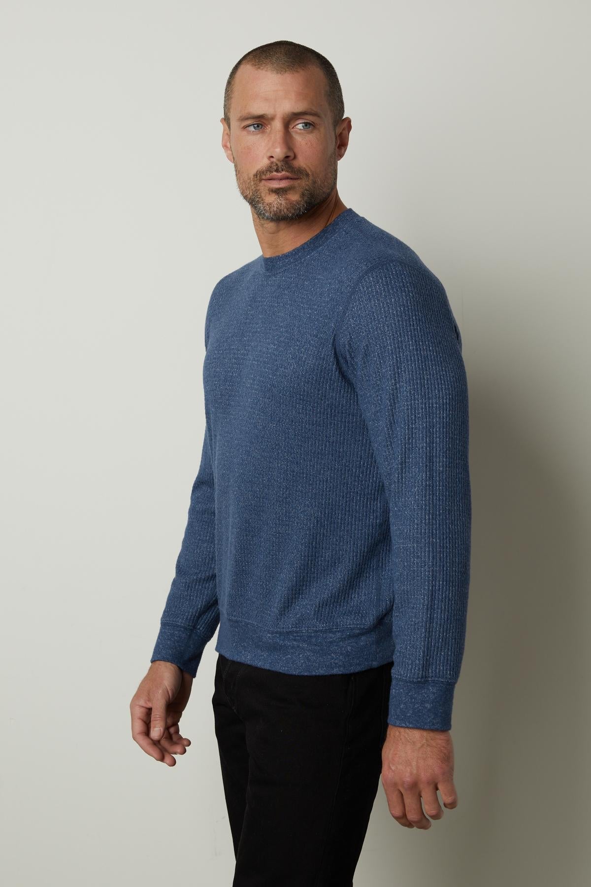   A man wearing a Velvet by Graham & Spencer PONCHO THERMAL CREW blue sweater on cooler days, paired with black pants. 