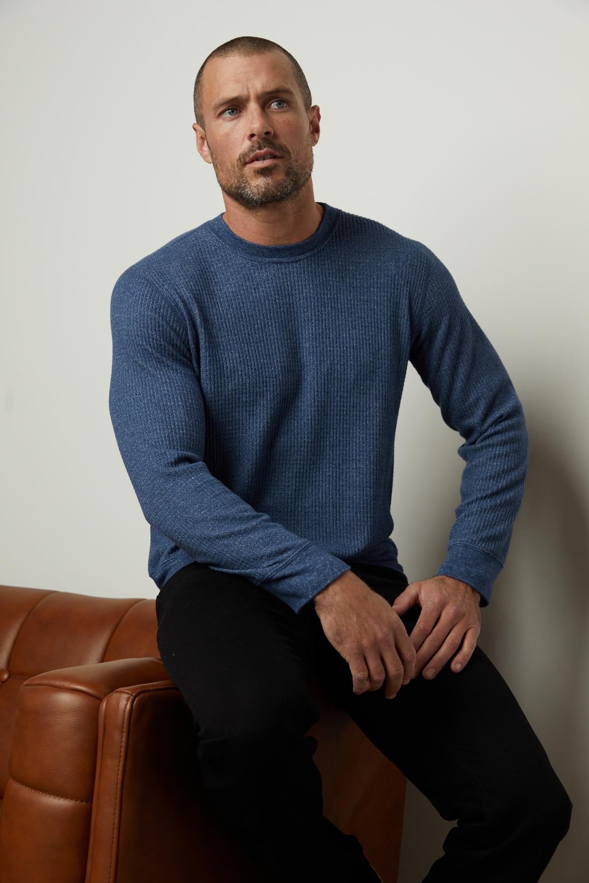   A man sitting on a couch wearing a Velvet by Graham & Spencer PONCHO THERMAL CREW, perfect for cooler days. 