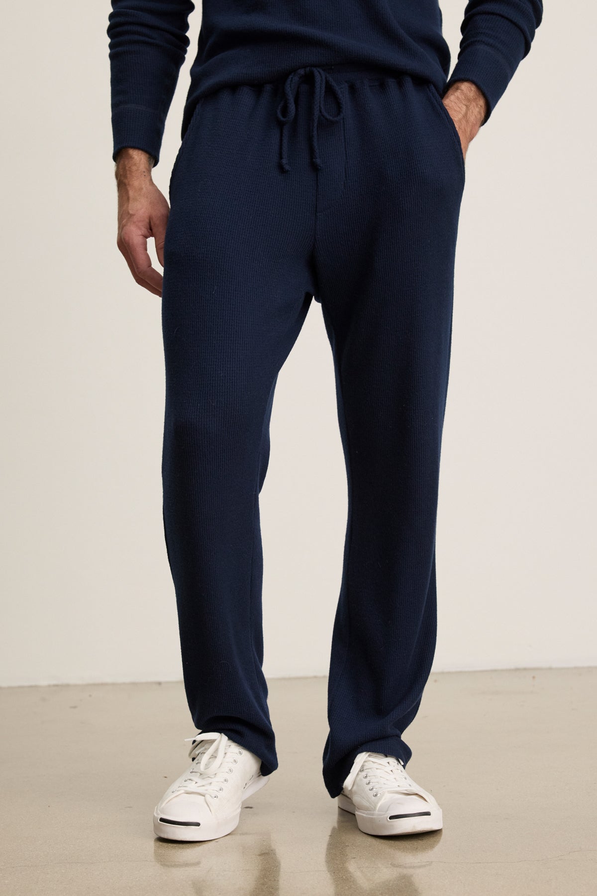 A person wearing Velvet by Graham & Spencer's OZZY SWEATPANT in navy blue with white sneakers stands on a light-colored floor against a plain background.-Hover Image