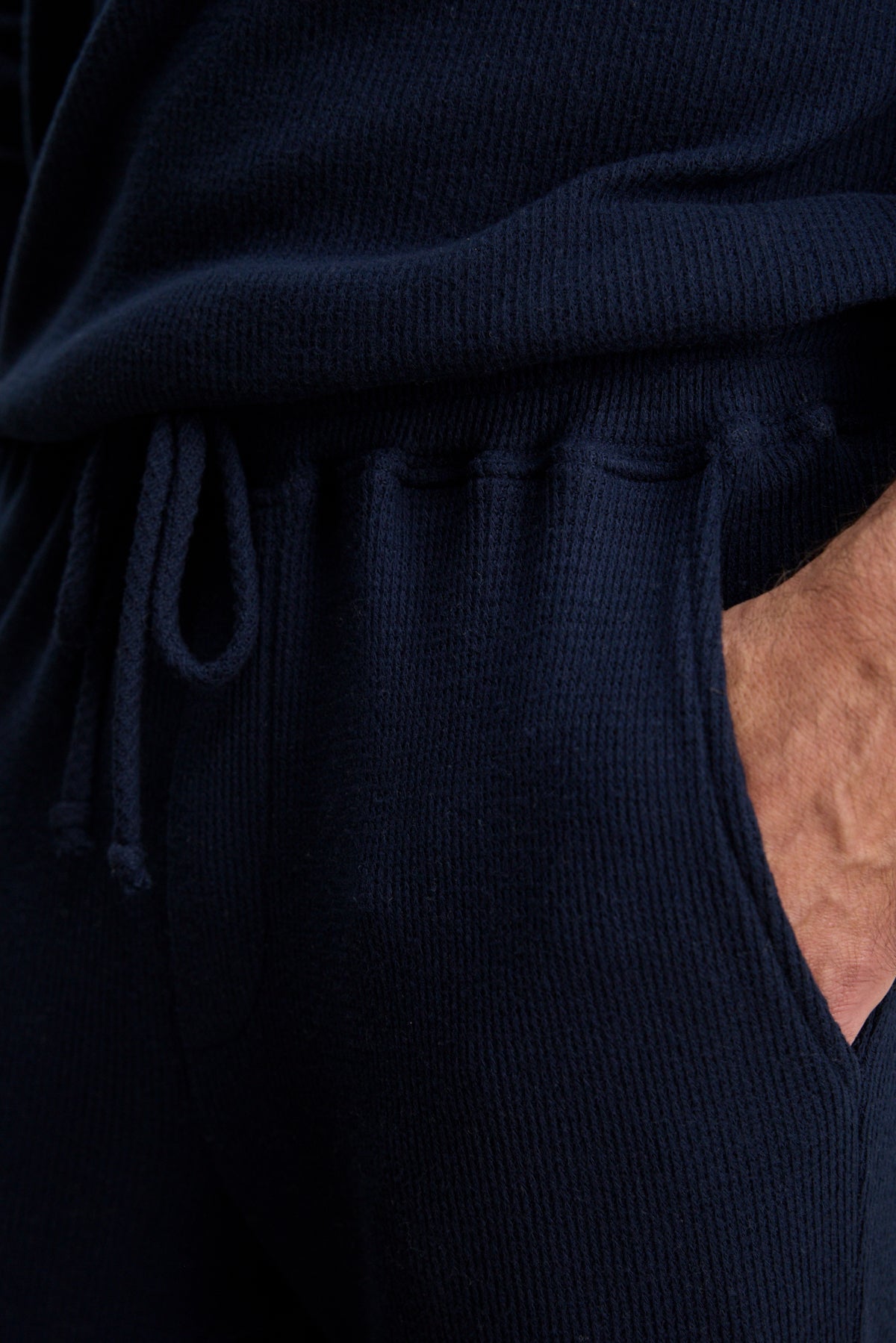 A person wearing a blue sweater and the OZZY SWEATPANT by Velvet by Graham & Spencer, featuring a relaxed fit and drawstring waist, with his hand in his pocket.-39957109801153