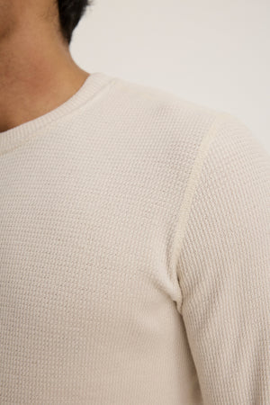 Close-up of a person wearing the TOBIAS CREW by Velvet by Graham & Spencer, featuring a textured off-white triblend thermal fabric with long sleeves, classic neckline, and visible shoulder seam.