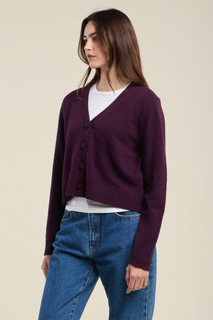A person wearing the ETNA CARDIGAN by Velvet by Graham & Spencer—a tailored fit, wool blend cardigan with a V-neckline—over a white shirt and blue jeans, standing against a plain light background.