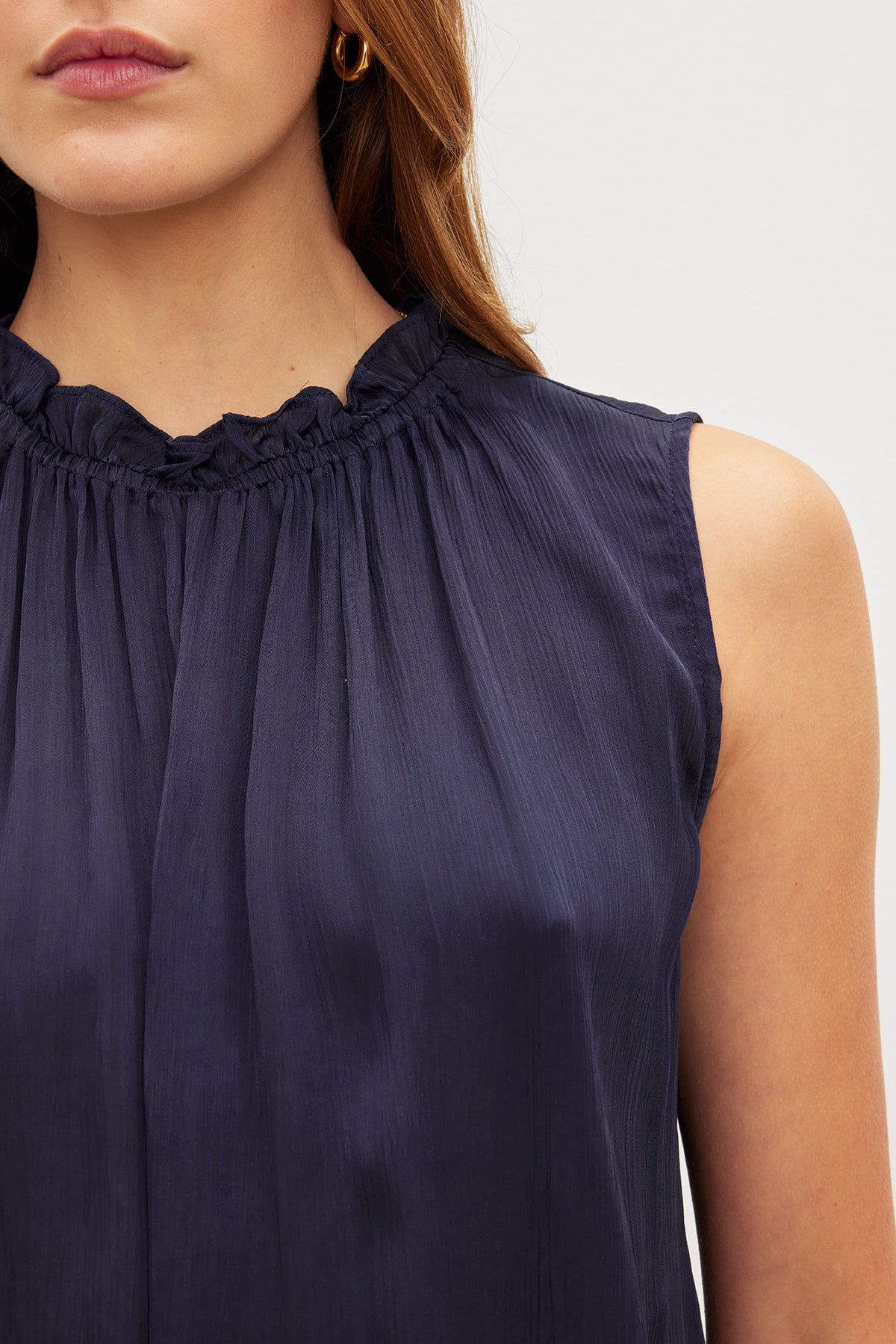 Close-up of a woman wearing a dark blue Velvet by Graham & Spencer Kiana Ruffle Neck Tank Top.-36409584189633