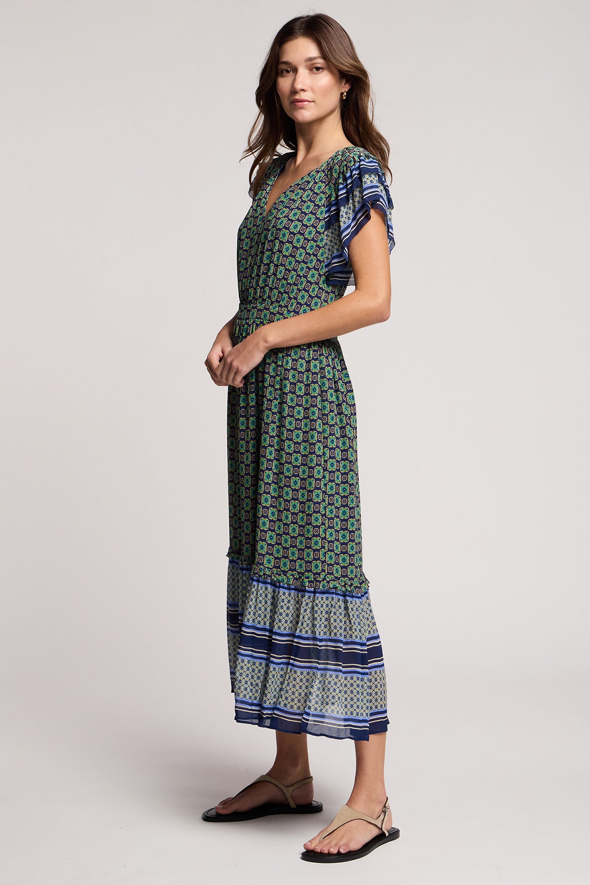 A woman models the CHERYL DRESS by Velvet by Graham & Spencer, featuring a bold border print, ruffled sleeves, and a tiered midi skirt—an ideal resort-ready look—styled with sandals against a plain background.-41526963142849