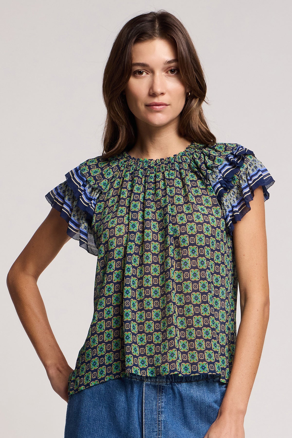 A woman wears the DAHLIA TOP by Velvet by Graham & Spencer—a short-sleeve crinkled viscose blouse with ruffled sleeves—paired with blue jeans, standing against a plain background.-41526968811713