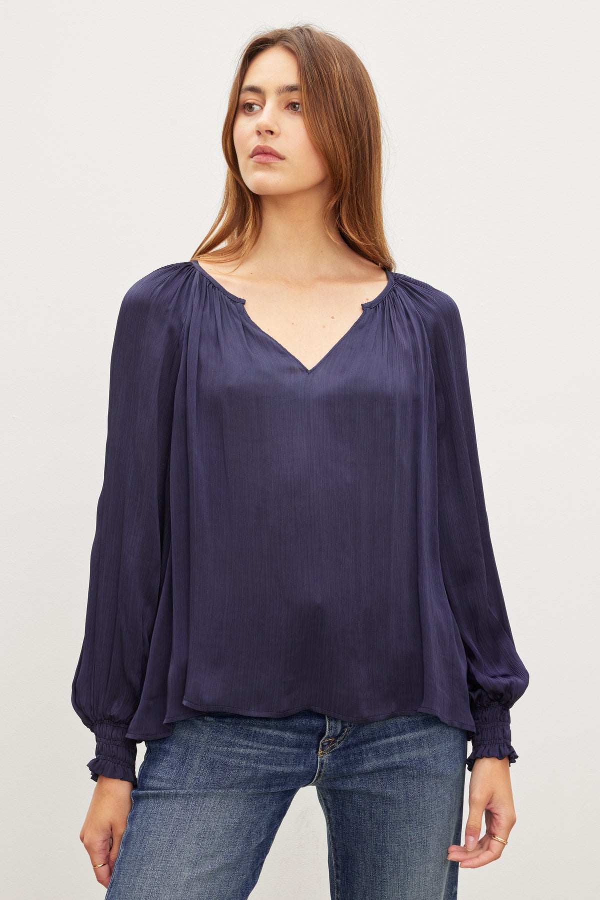   A person with long hair wearing a loose, dark blue HELEN TOP by Velvet by Graham & Spencer and blue jeans stands against a plain background. 