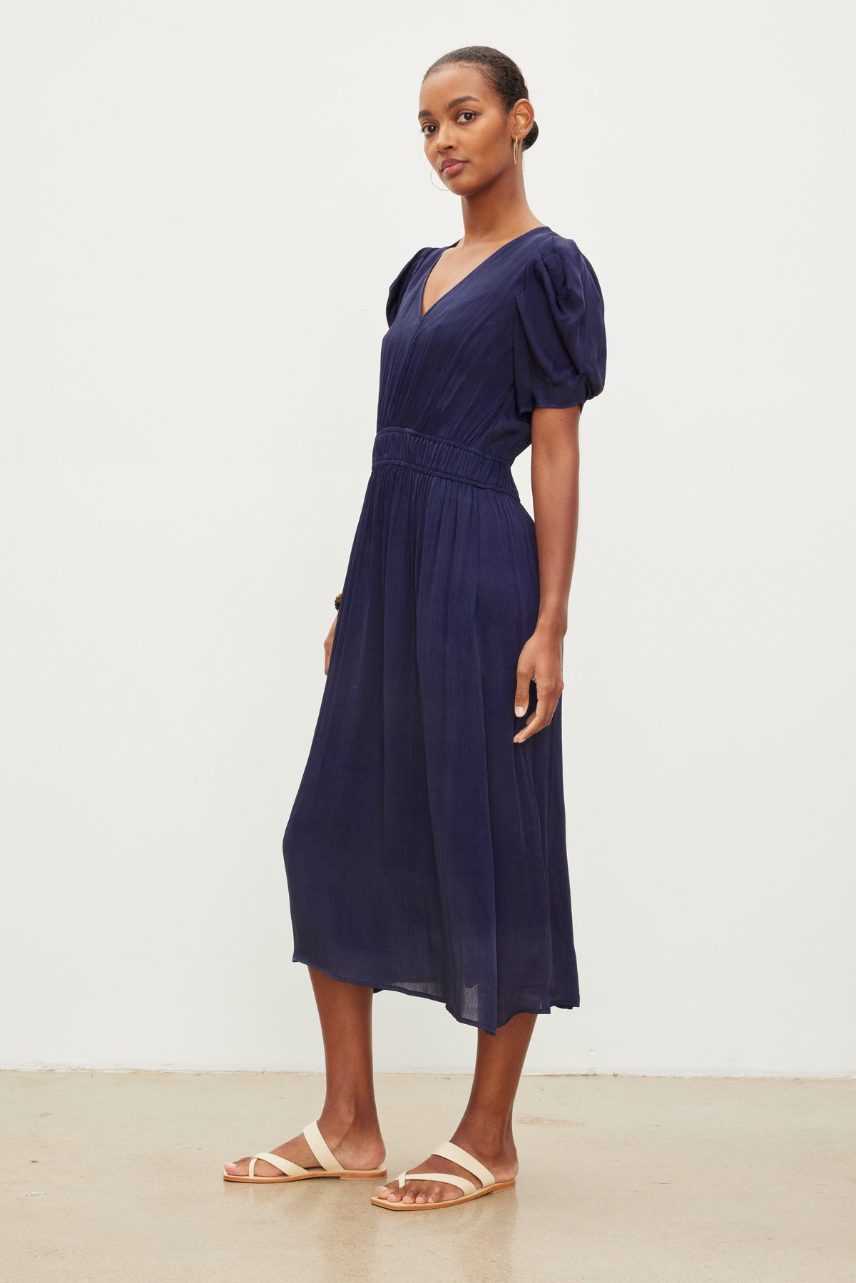   A person stands against a plain white background, wearing the JOSEY DRESS by Velvet by Graham & Spencer with short puffed sleeves and beige flat sandals. 