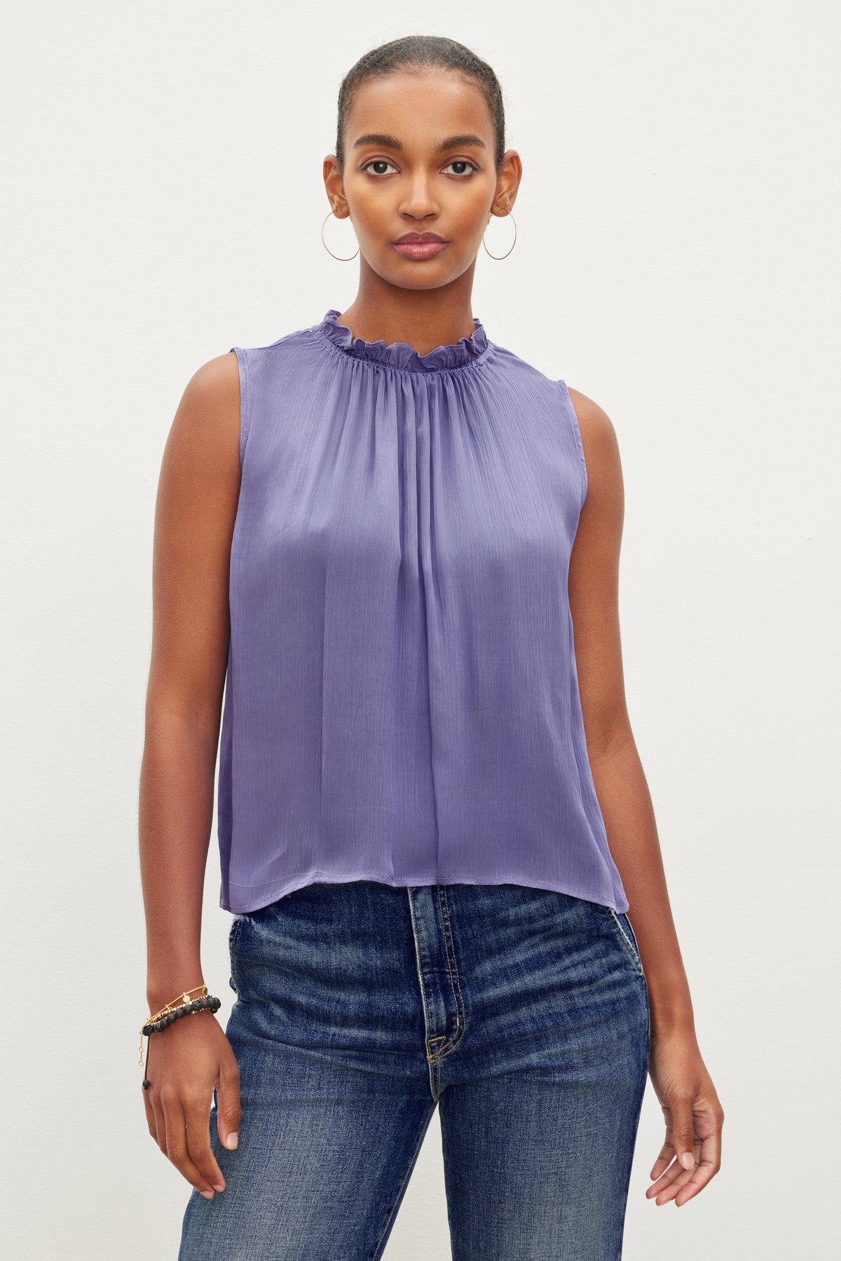   A person stands against a plain background, wearing the Velvet by Graham & Spencer KIANA RUFFLE NECK TANK TOP and blue jeans. 