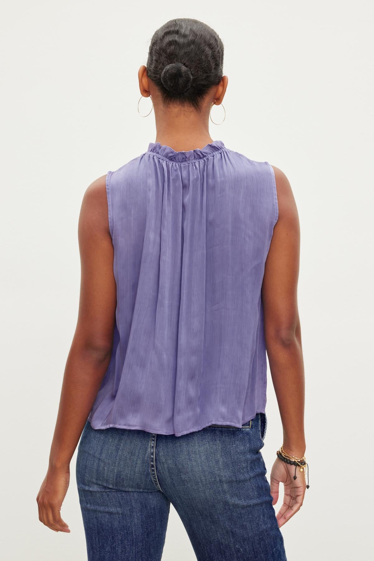   A person is wearing a purple KIANA RUFFLE NECK TANK TOP by Velvet by Graham & Spencer and blue jeans, photographed from the back. 