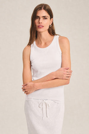 A woman stands against a neutral background wearing the CRUZ TANK TOP by Velvet by Jenny Graham and a white drawstring skirt—versatile essentials ideal for any capsule wardrobe.
