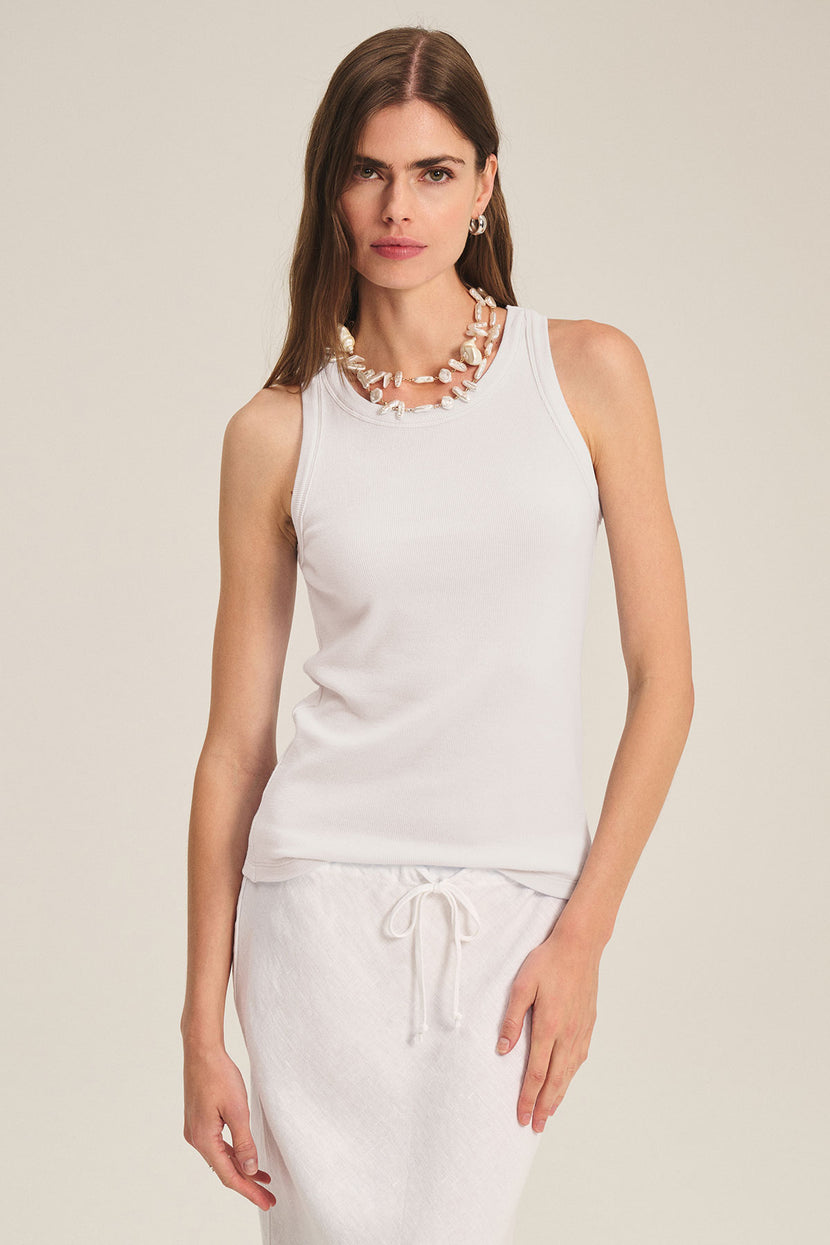 A woman wears the CRUZ TANK TOP by Velvet by Jenny Graham and a white drawstring skirt, styled with a chunky necklace—an essential look for any capsule wardrobe. She stands against a plain background.