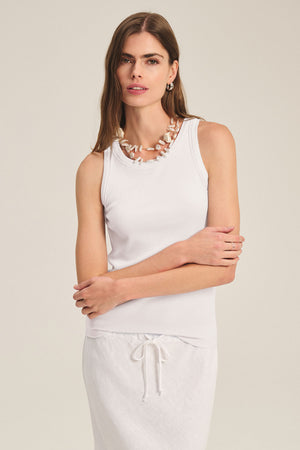 A woman wears the CRUZ TANK TOP by Velvet by Jenny Graham with a white drawstring skirt, large bead necklace, and hoop earrings, standing against a plain background—an effortless capsule wardrobe look.