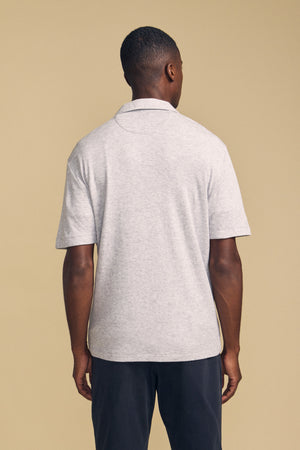 A person stands facing away from the camera, wearing the Velvet by Graham & Spencer FOX POLO in light gray paired with dark pants, set against a plain beige background.