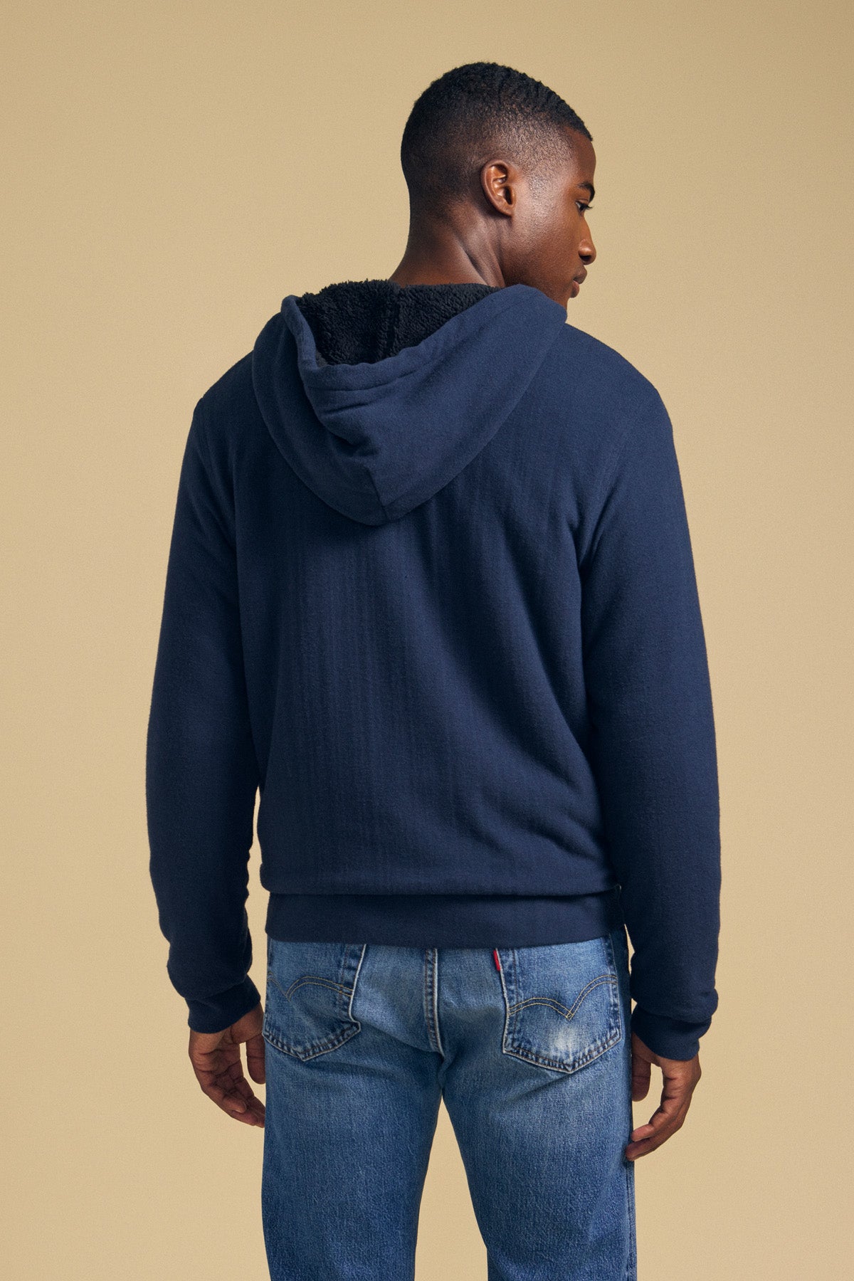 A person viewed from behind wearing a dark blue CARTER FULL-ZIP HOODIE and blue jeans.