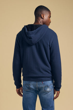 A person viewed from behind wearing a dark blue CARTER FULL-ZIP HOODIE and blue jeans.