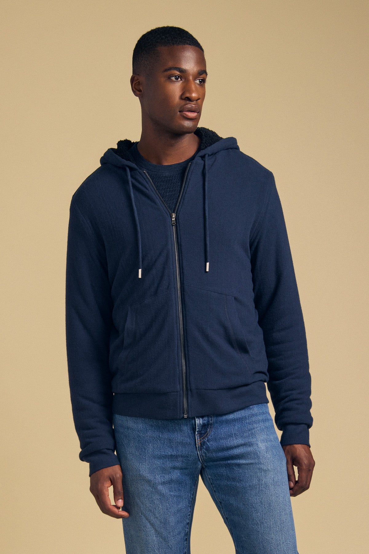 A man wearing a navy blue CARTER FULL-ZIP HOODIE over a dark shirt and blue jeans.
