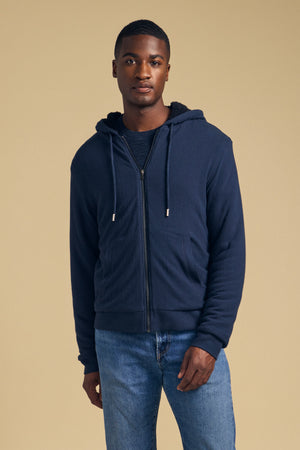 A man wearing a navy blue CARTER FULL-ZIP HOODIE over a dark shirt and blue jeans.