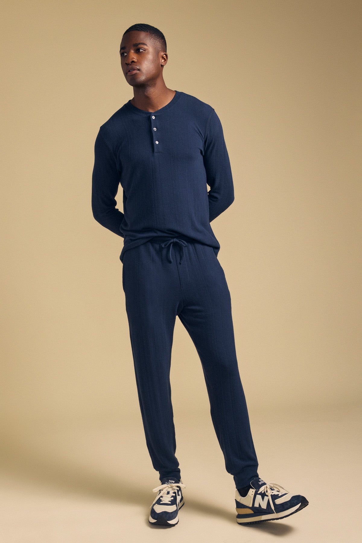 A man wearing a relaxed fit navy cotton jersey henley and matching ELLIS SWEATPANT by Velvet by Graham & Spencer with athletic sneakers.