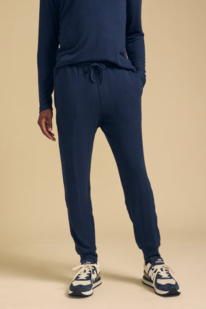 A person wearing navy blue cotton jersey ELLIS SWEATPANTs by Velvet by Graham & Spencer with a drawstring waist and navy and white athletic shoes.