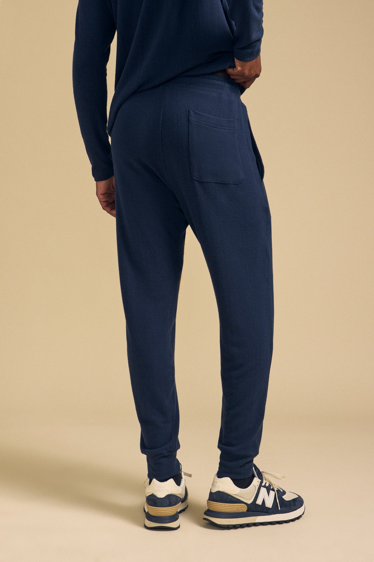A person seen from behind, wearing dark blue cotton jersey ELLIS SWEATPANT by Velvet by Graham & Spencer with a back pocket and blue and white sneakers.