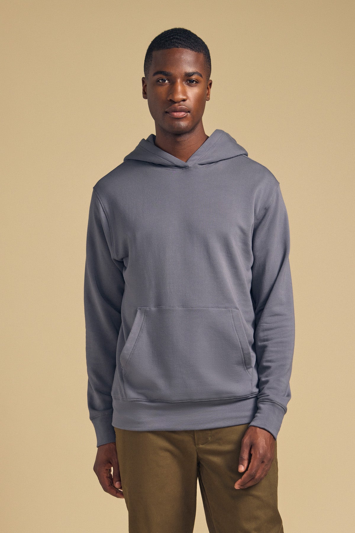 A person stands facing forward against a beige background, wearing the EVERSON HOODIE in gray from Velvet by Graham & Spencer paired with olive-green pants, showcasing a modern wardrobe essential.