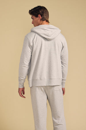 A person stands with their back to the camera, wearing the GUS HOODIE and matching sweatpants by Velvet by Graham & Spencer in light gray, set against a plain beige background.