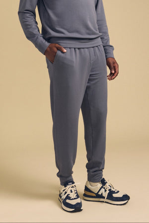 A person wearing the Velvet by Graham & Spencer JACOBY JOGGER and a matching gray sweatshirt, with hands in pockets and navy and beige sneakers, stands against a plain beige background.