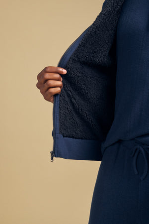 A person wearing a navy blue Velvet by Graham & Spencer NASH JACKET with a mock neck, full-zip closure, and a dark faux sherpa interior lining.