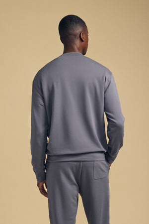 A person is standing with their back to the camera, wearing the gray OTIS SWEATSHIRT by Velvet by Graham & Spencer and matching gray relaxed-fit pants against a beige background.