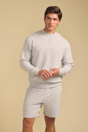 A man stands against a beige background wearing the light gray OTIS SWEATSHIRT by Velvet by Graham & Spencer with matching shorts.