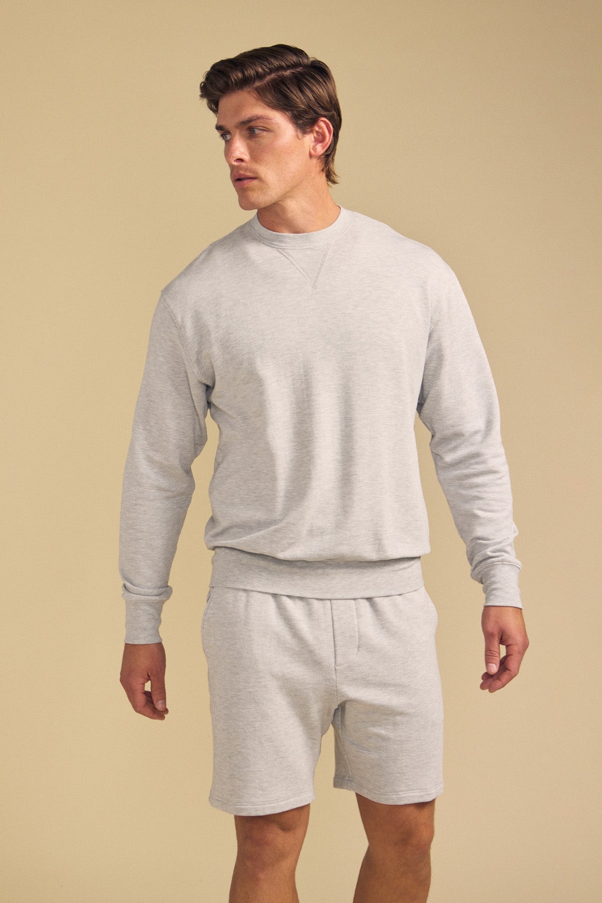 A man wearing the OTIS SWEATSHIRT by Velvet by Graham & Spencer, paired with matching shorts, stands against a plain beige background and looks to his left.-41702161416385