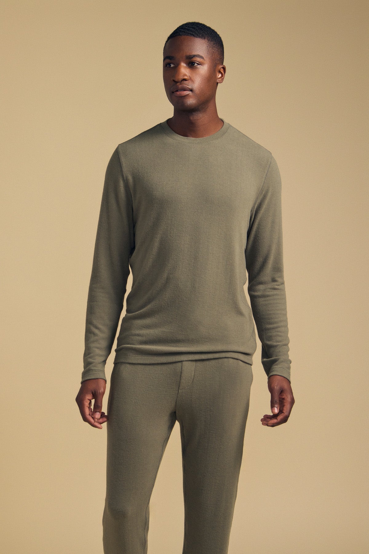 A man stands against a beige background wearing the REDDEN CREW PULLOVER by Velvet by Graham & Spencer in matching olive green, paired with coordinating pants. Crafted from cozy jersey for everyday comfort, he looks slightly to the side with his hands relaxed at his sides.