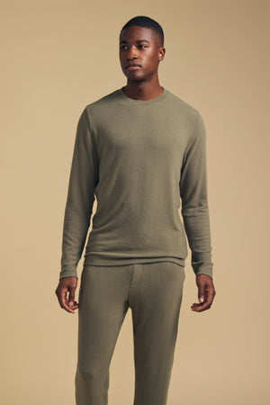A man stands against a beige background wearing the REDDEN CREW PULLOVER by Velvet by Graham & Spencer in matching olive green, paired with coordinating pants. Crafted from cozy jersey for everyday comfort, he looks slightly to the side with his hands relaxed at his sides.